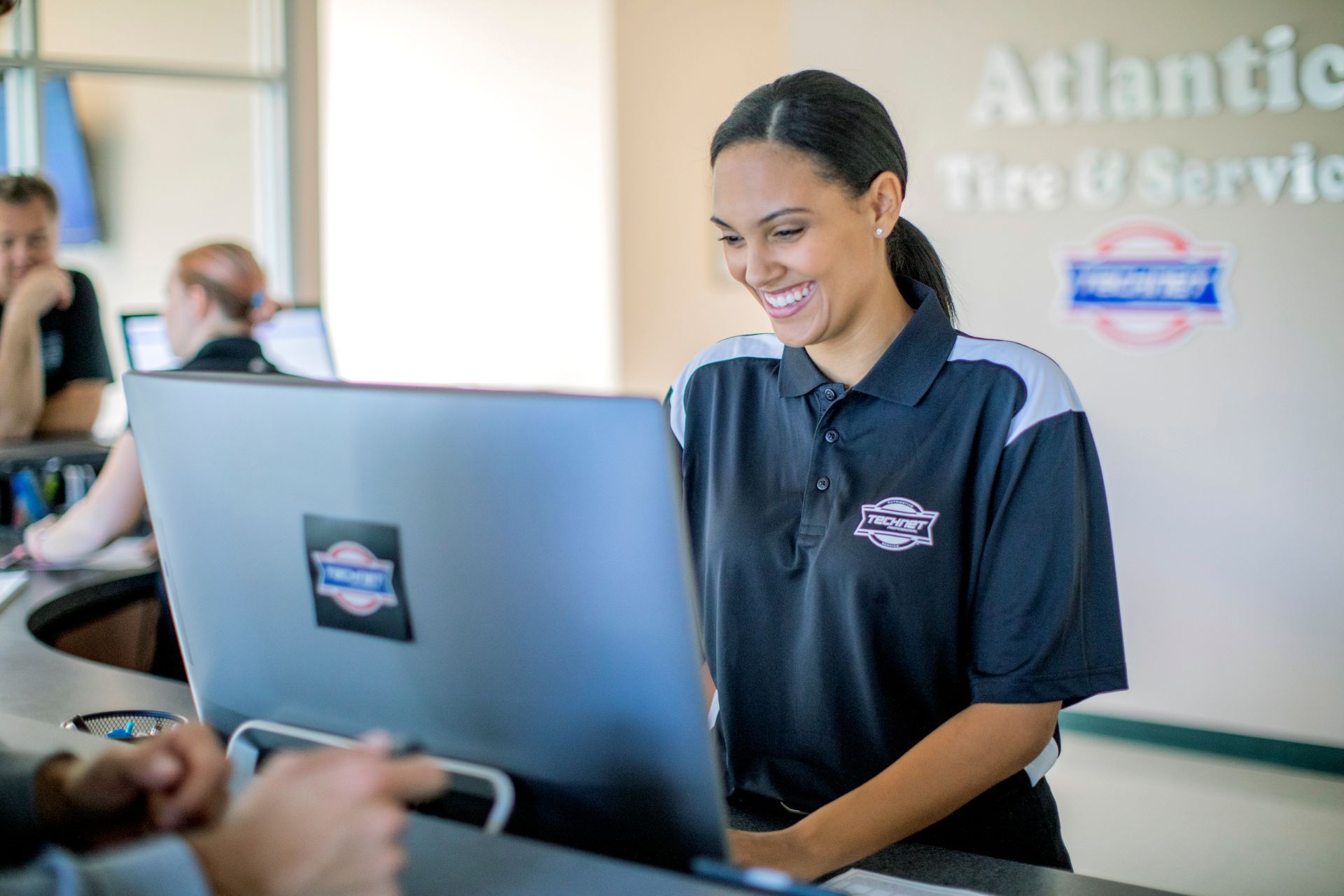 A woman is working on a laptop in front of a sign that says atlantic tire & service