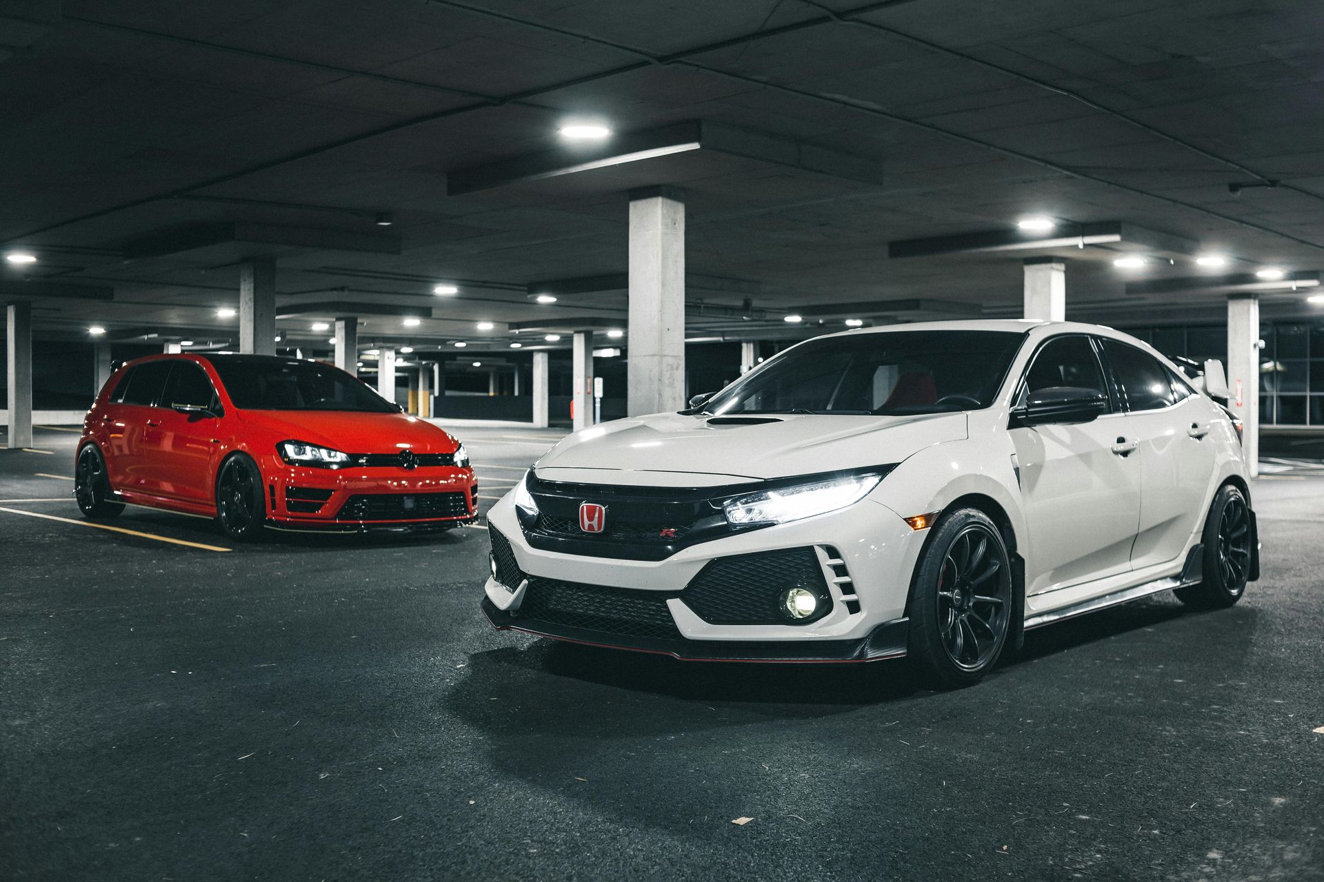 White sports hatchback and red sedan parked in a dim underground garage.