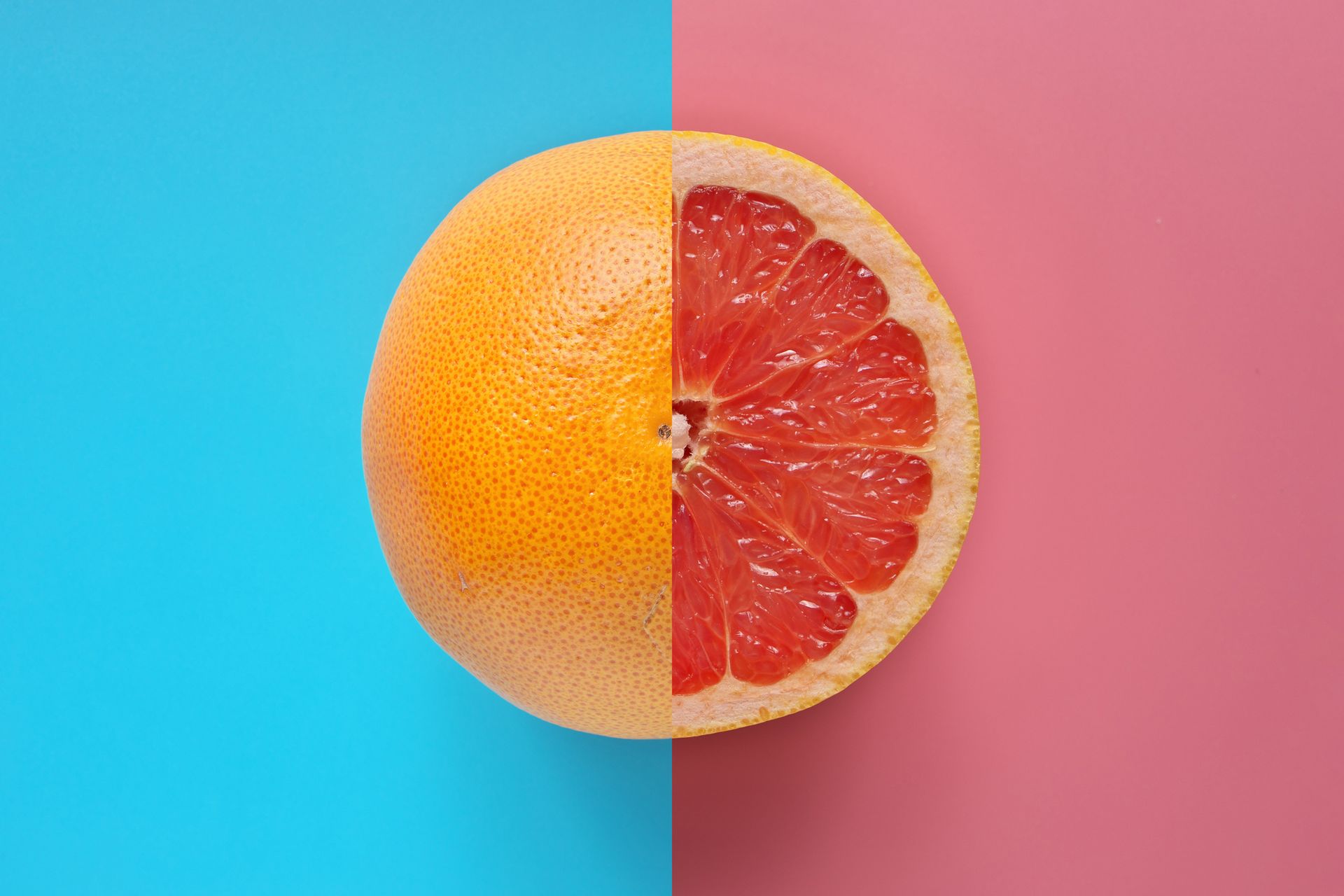 Half grapefruit, whole on the left, cut side on the right, on blue and pink backgrounds.