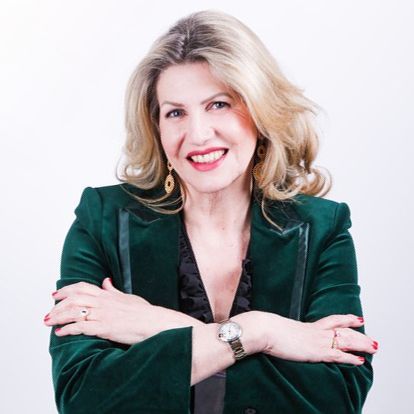 Woman with blonde hair, emerald green blazer, arms crossed, smiling, and looking directly at the camera.