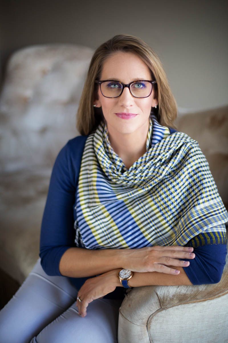 Woman wearing glasses and scarf, sitting on a couch.
