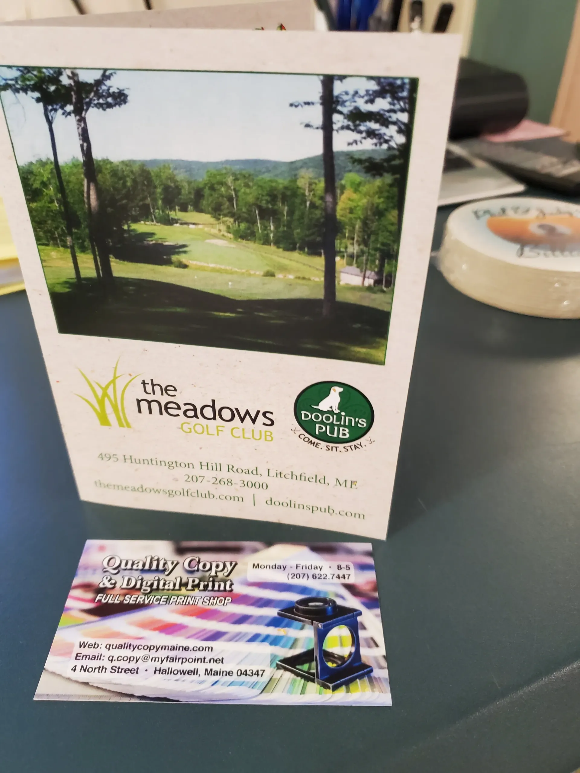 A card with a golf course image and a business card on a desk.
