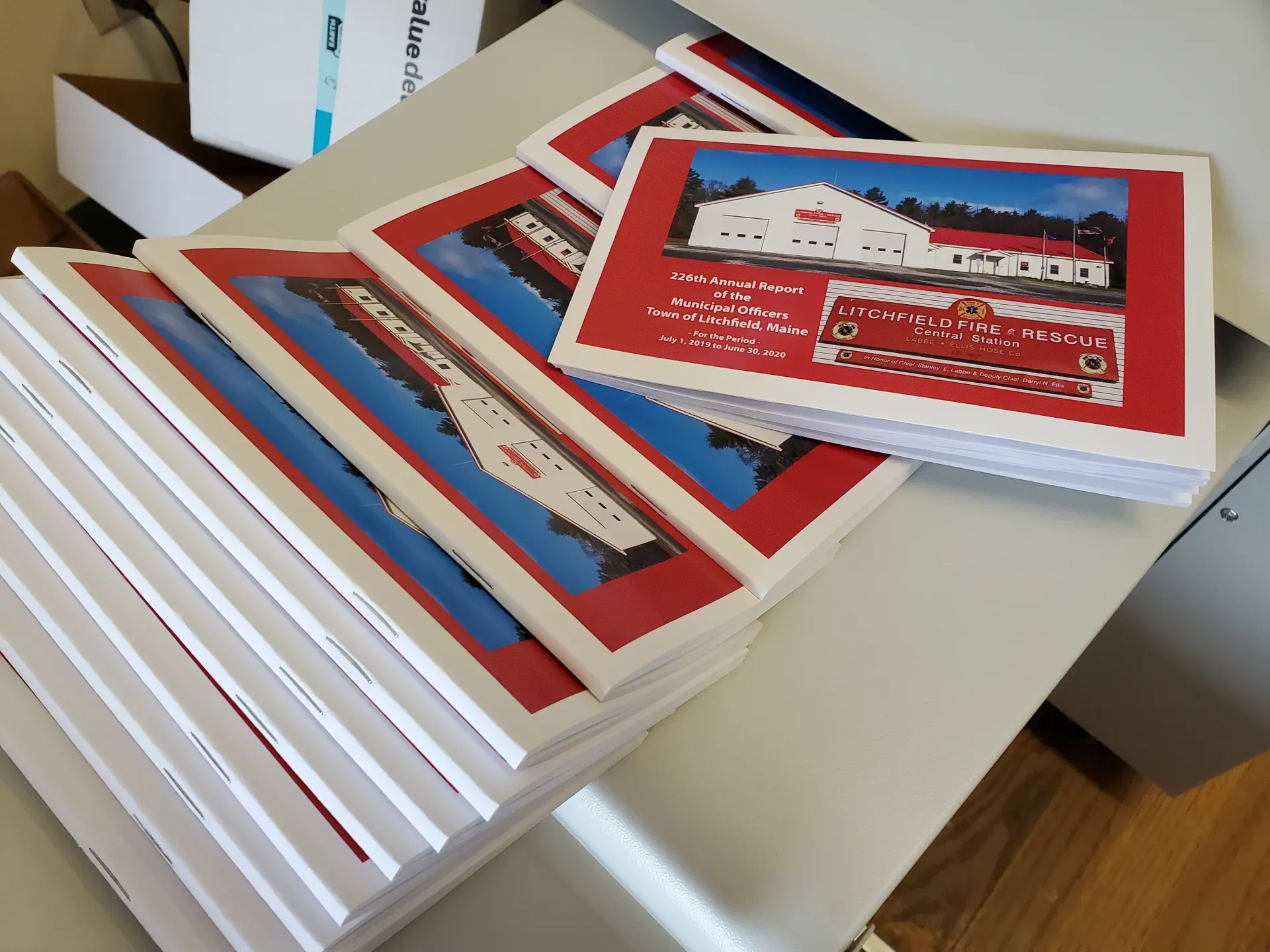 Stacks of prints with red borders, featuring a tram and building, on a white table.