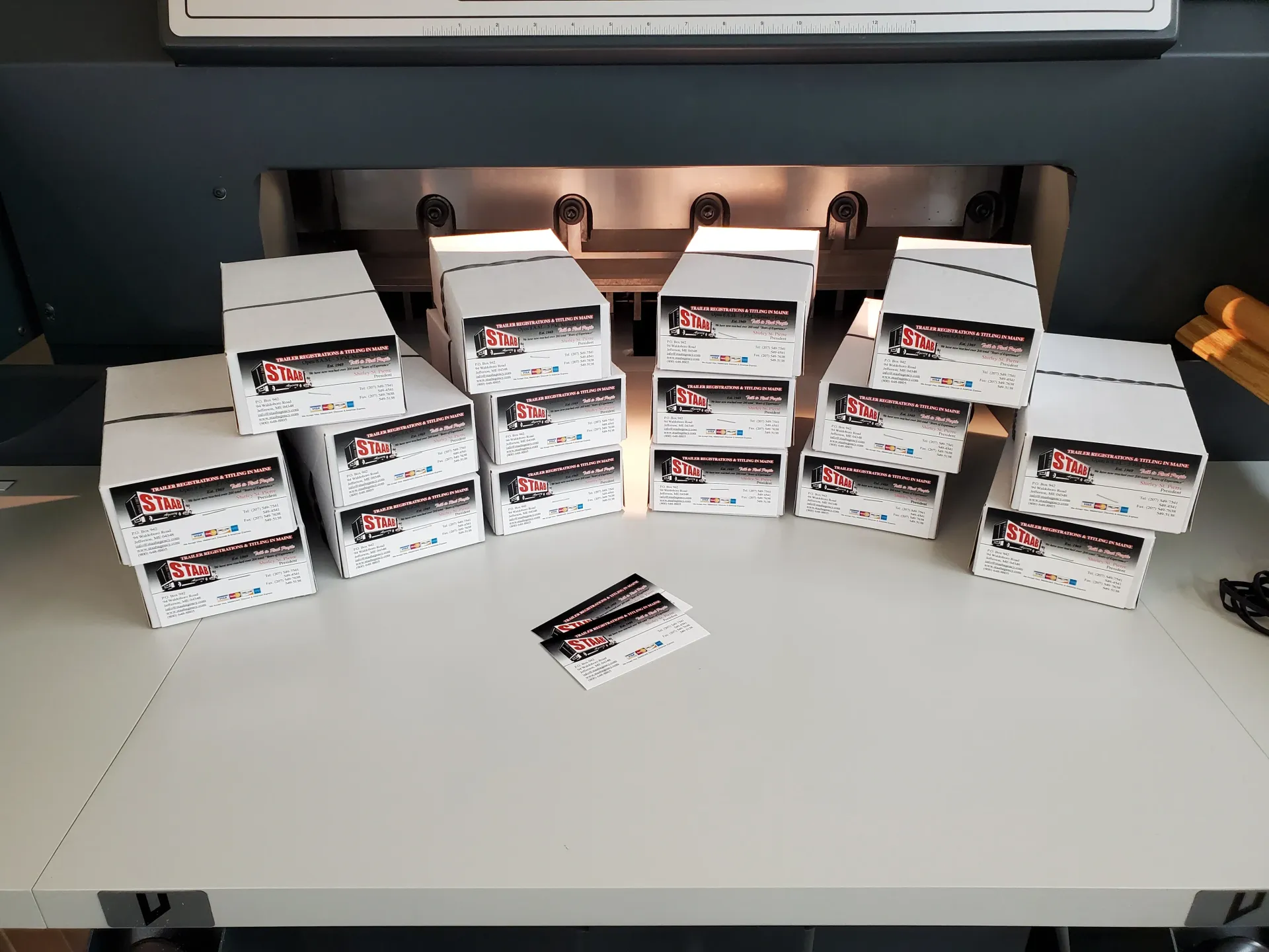 Stacks of white boxes with red logos on a table in front of a paper cutter.