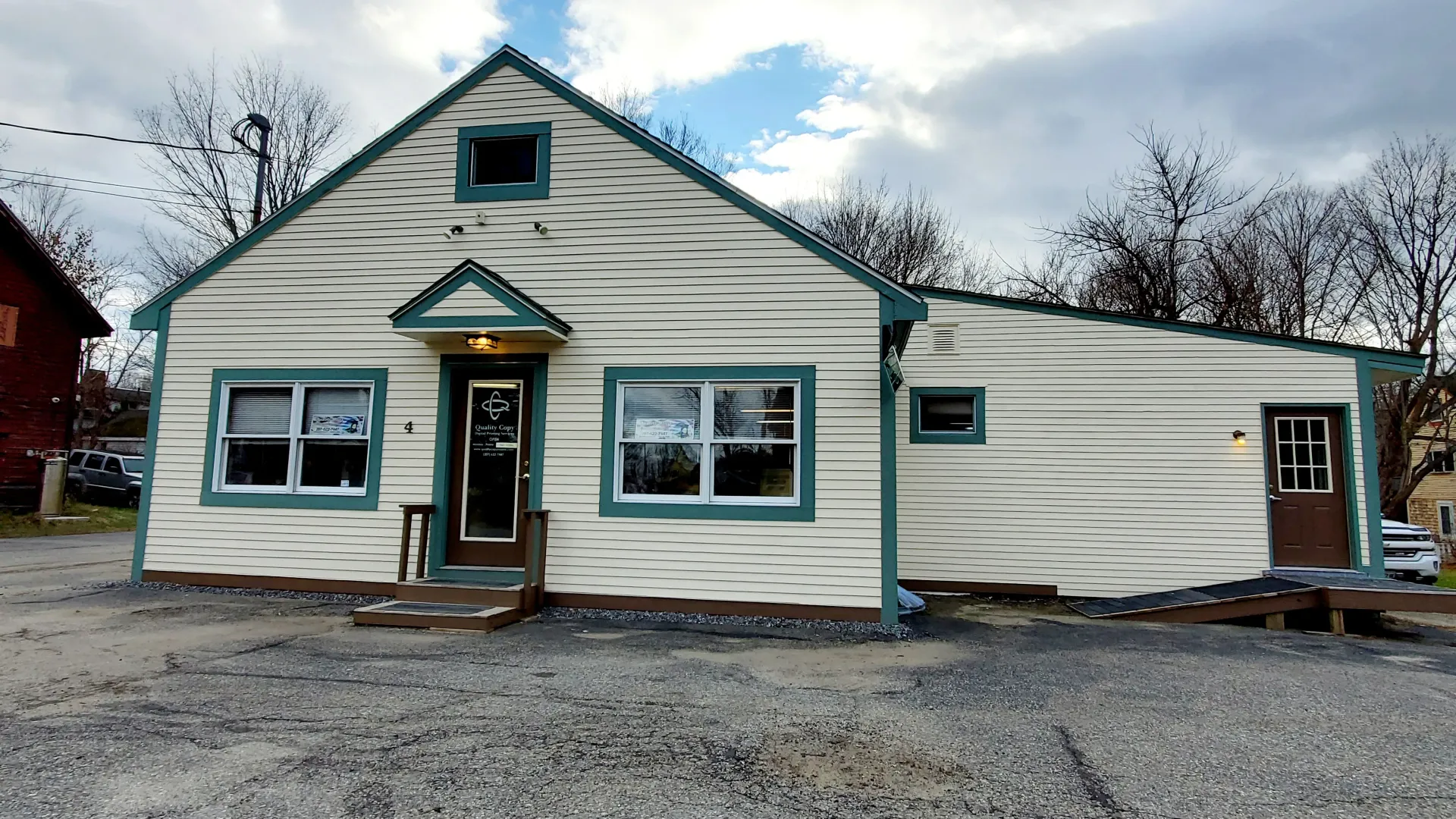 Beige house with teal trim, windows, and a door, cloudy sky.