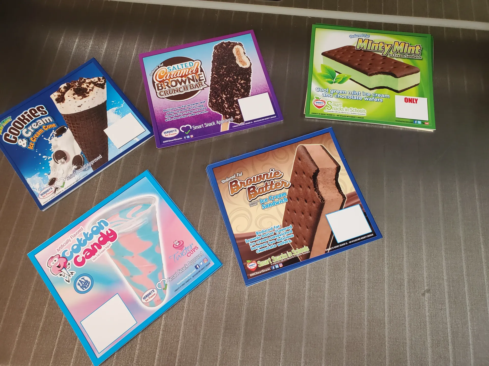 Five boxes of ice cream: cone, bar, sandwich, cotton candy, and brownie flavor, on a shiny surface.