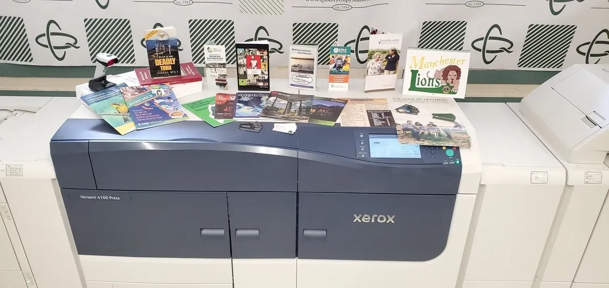 A printer topped with various cards and figurines. White walls with green and white geometric shapes in the background.