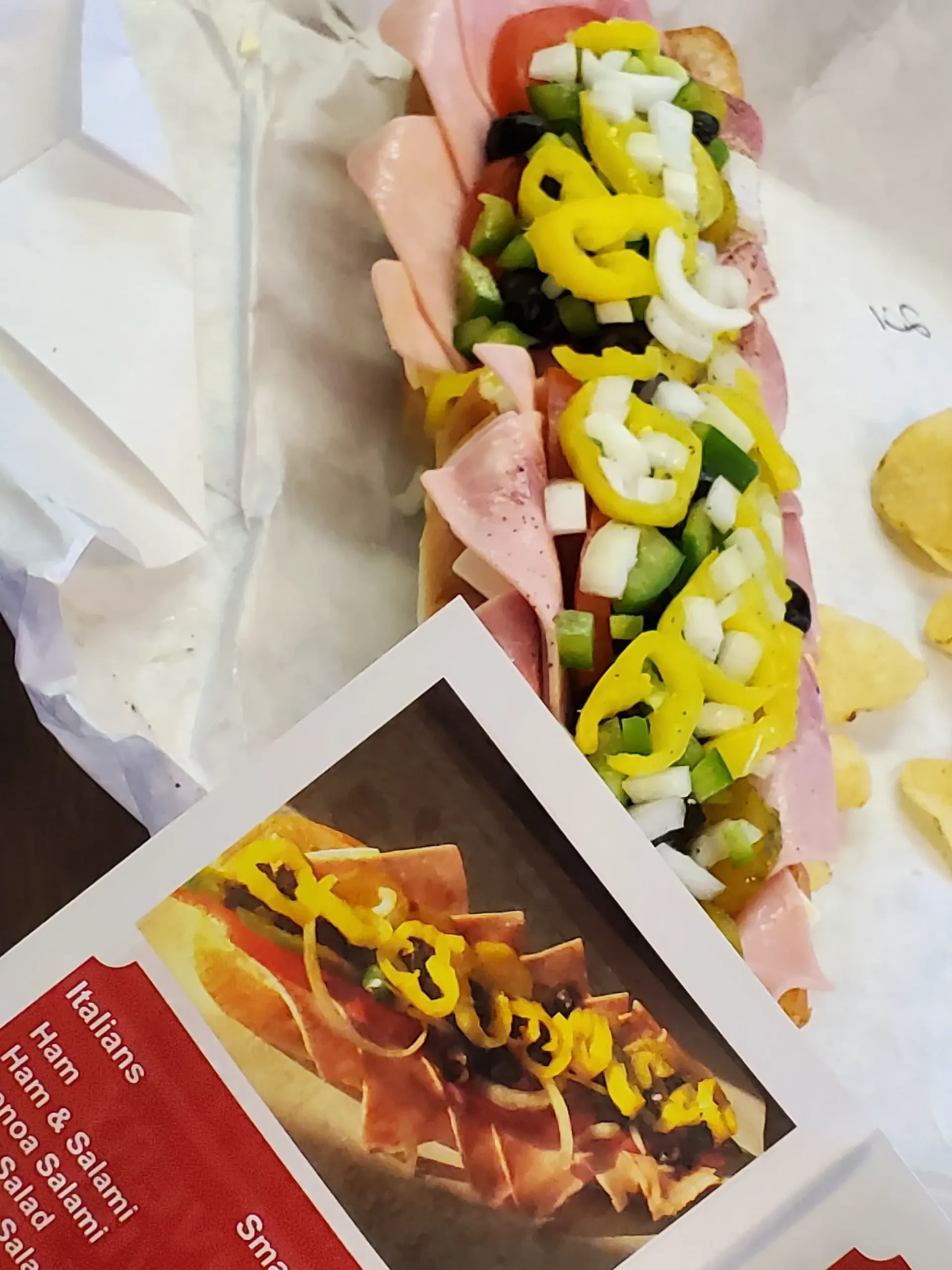 Italian sub sandwich with ham, salami, and vegetables, next to a menu.