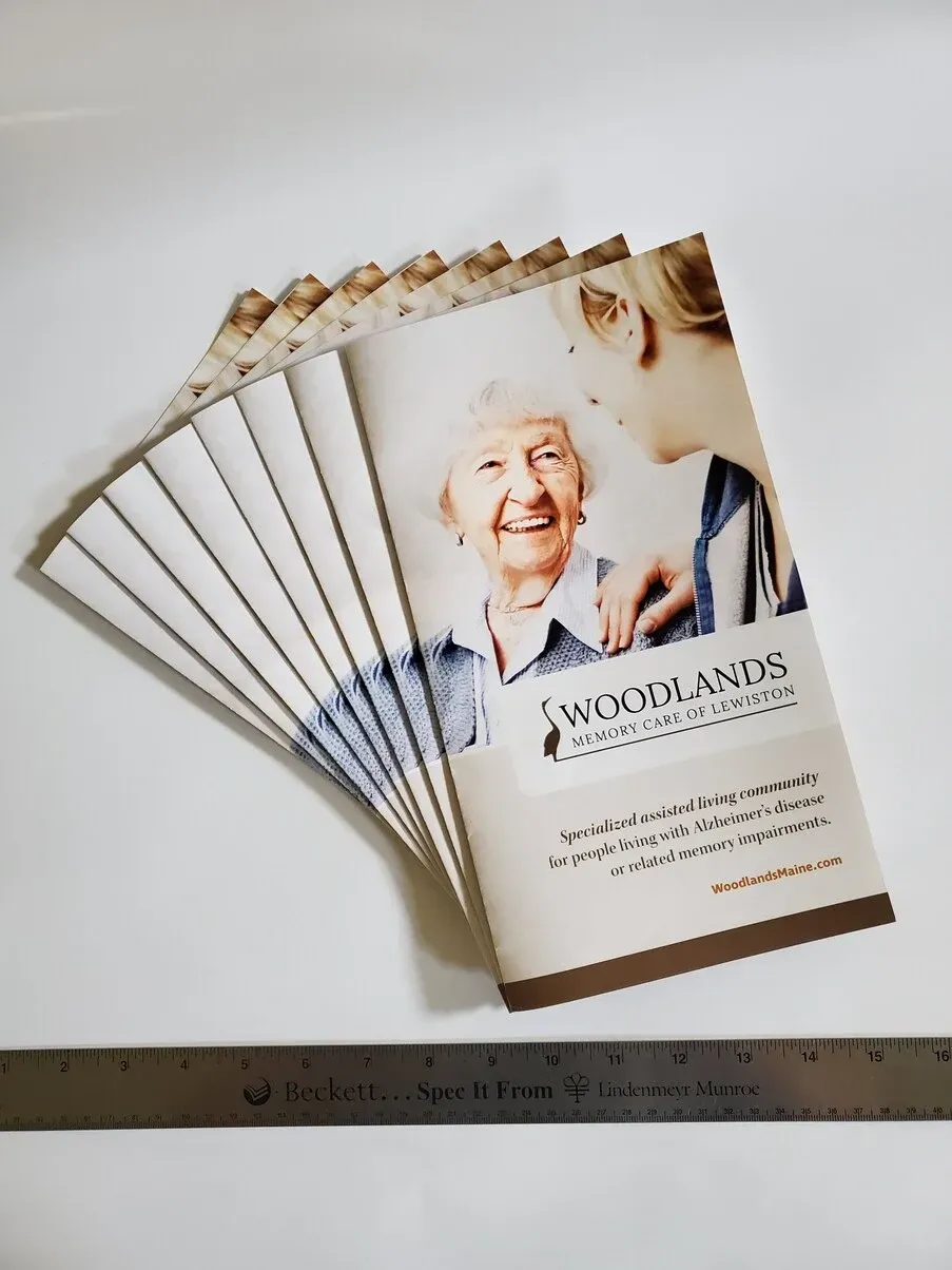 Brochures for Woodlands, an assisted living facility, fanned out. The cover features an elderly woman smiling, with a caregiver.