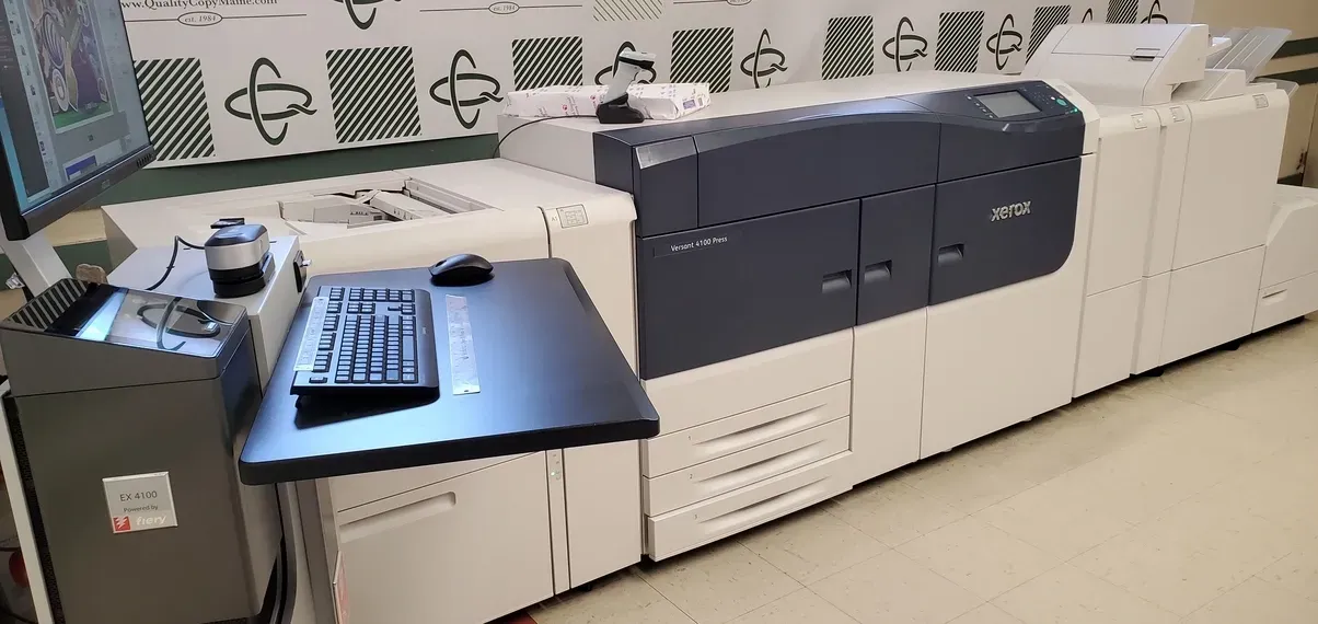 A large printing machine with a computer setup, indoors.