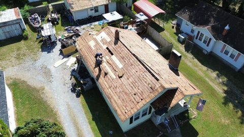 An aerial view shows a person on a house roof undergoing repairs, with missing shingles, debris, and tools visible.