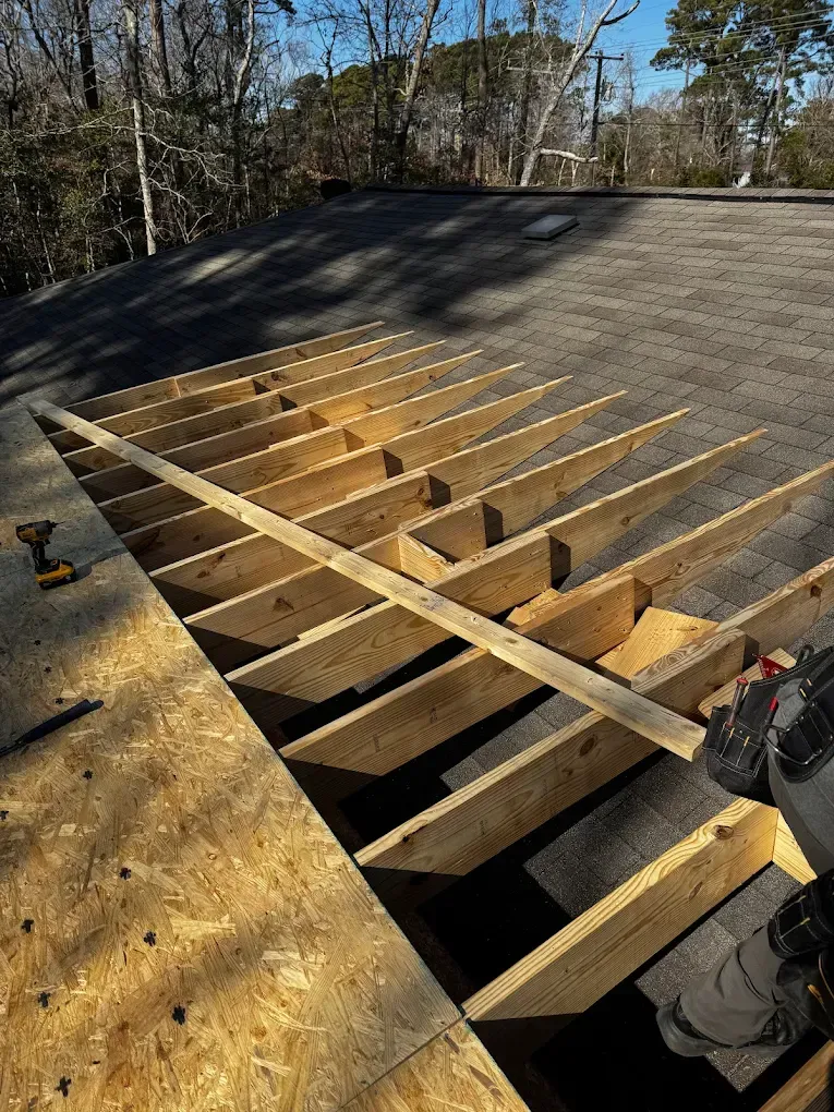 Roof under renovation with exposed wooden rafters and tools on a shingled roof