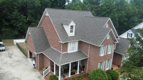 An aerial view of a two-story red brick house with a gray shingle roof, white trim, and a wrap-around porch.