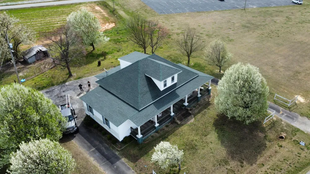 Aerial view of a white house with a dark roof, surrounded by trees and open yard.