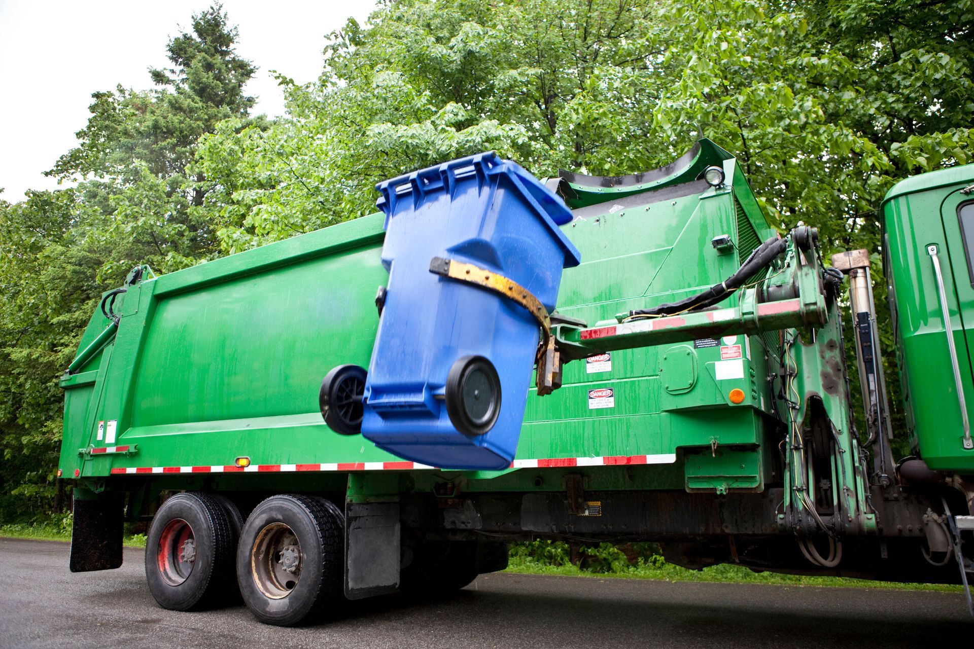 Garbage truck lifting a blue waste bin with its mechanical arm during trash collection.