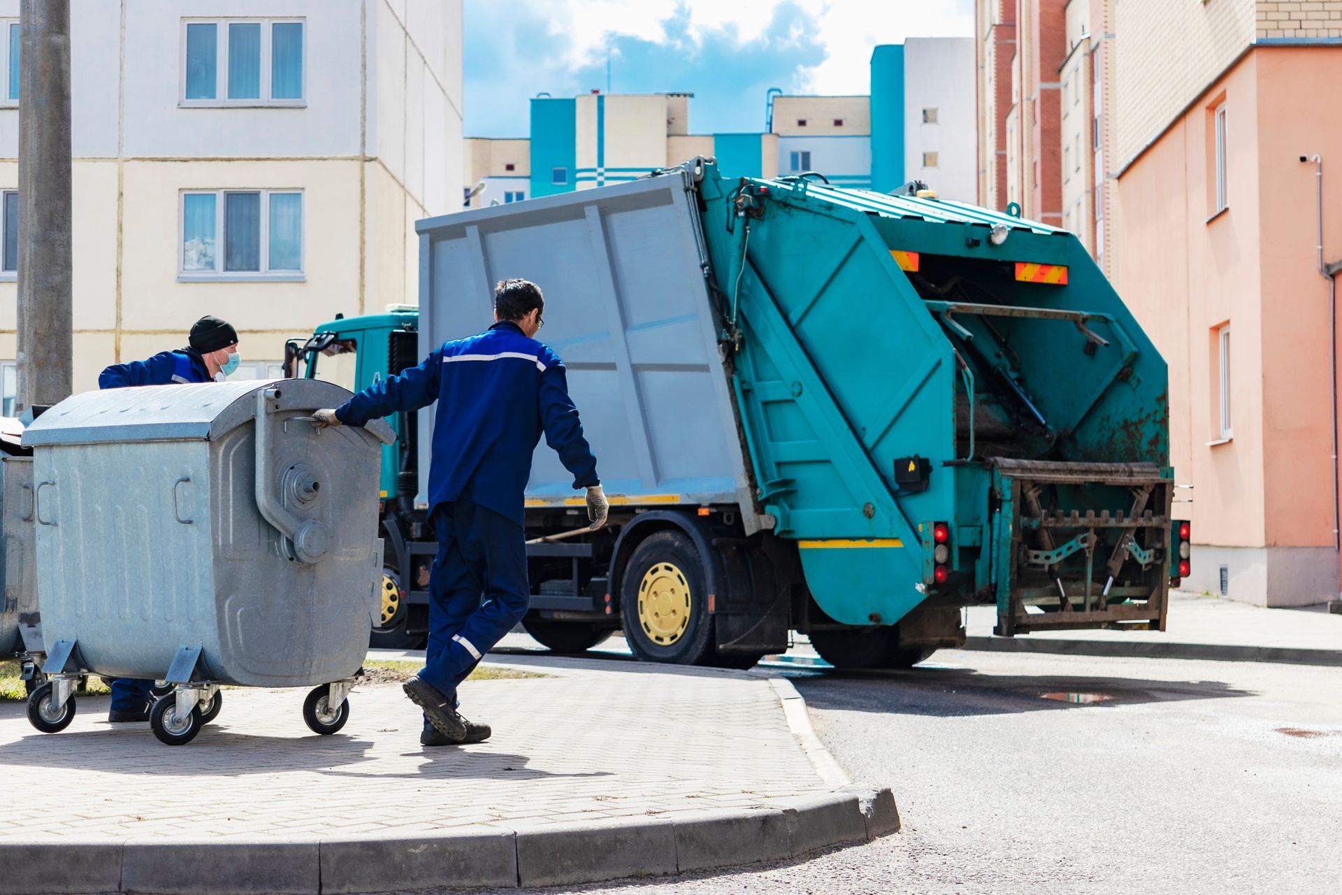 two sanitation workers collecting trash in a residential area with a green garbage truck parked.