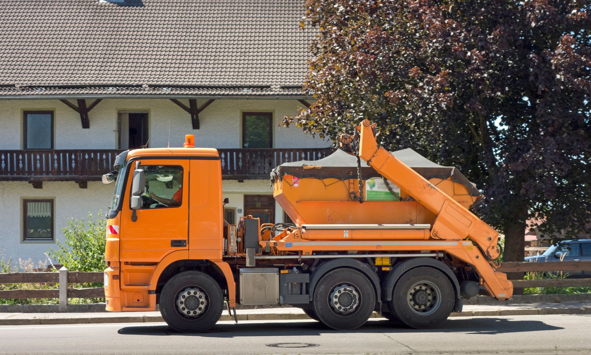Orange construction truck hauling container parked on street near residential home.