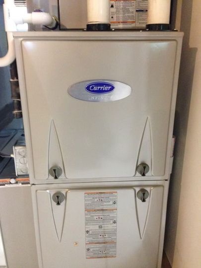 A Carrier furnace in a home setting, cream-colored with a central logo, two access panels.