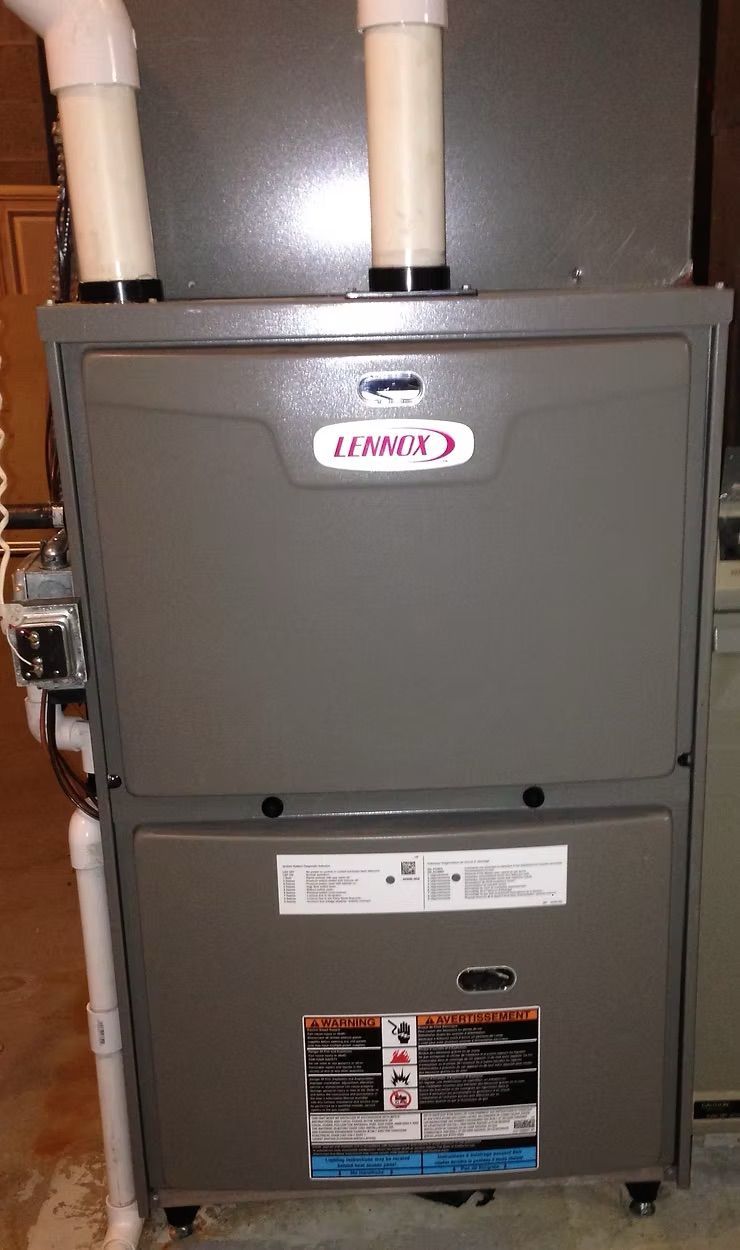 Lennox furnace with white vent pipes. Gray metal casing, mounted in a utility room.