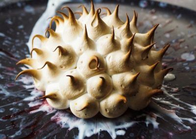 Toasted meringue dessert on a dark plate with sauce.