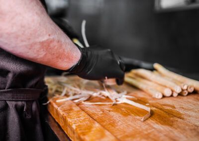 Chef peeling white asparagus on a wooden cutting board, wearing a black glove.