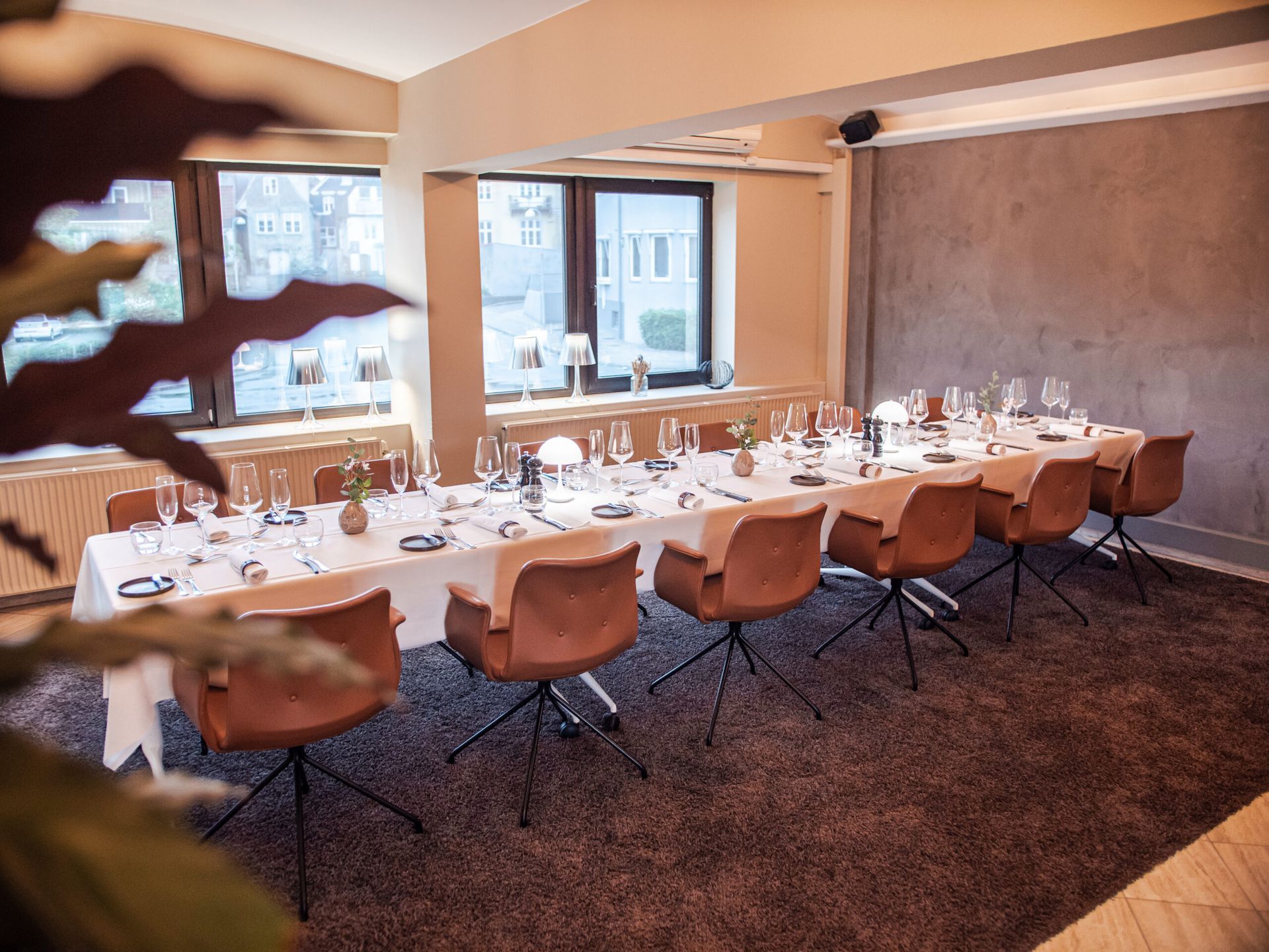 Long table set for a meal, with chairs, glassware, and decor in a restaurant dining room.