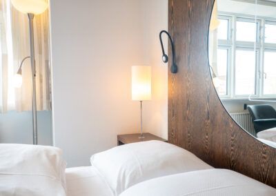 Bedroom interior with bed, lamp, mirror, and window.