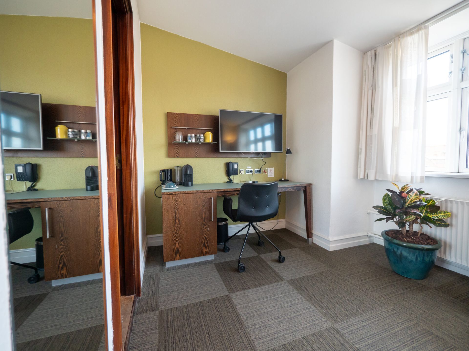 Home office with desk, TV, computer, chair, and potted plant. Beige, brown, and green color scheme.