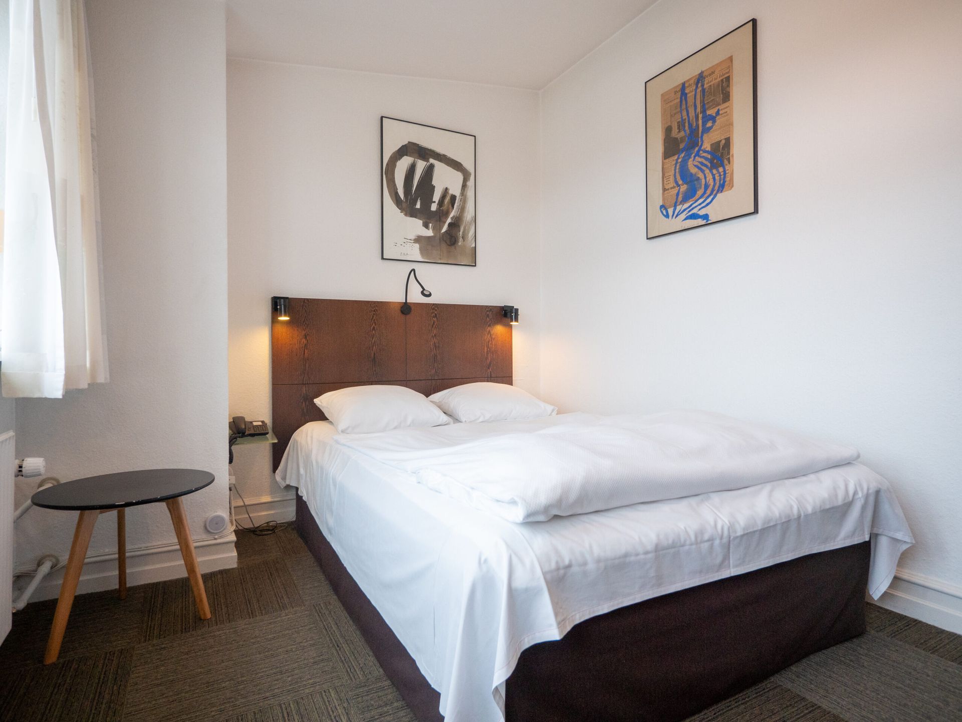 Cozy hotel bedroom with a double bed, two abstract art pieces, and a small table.