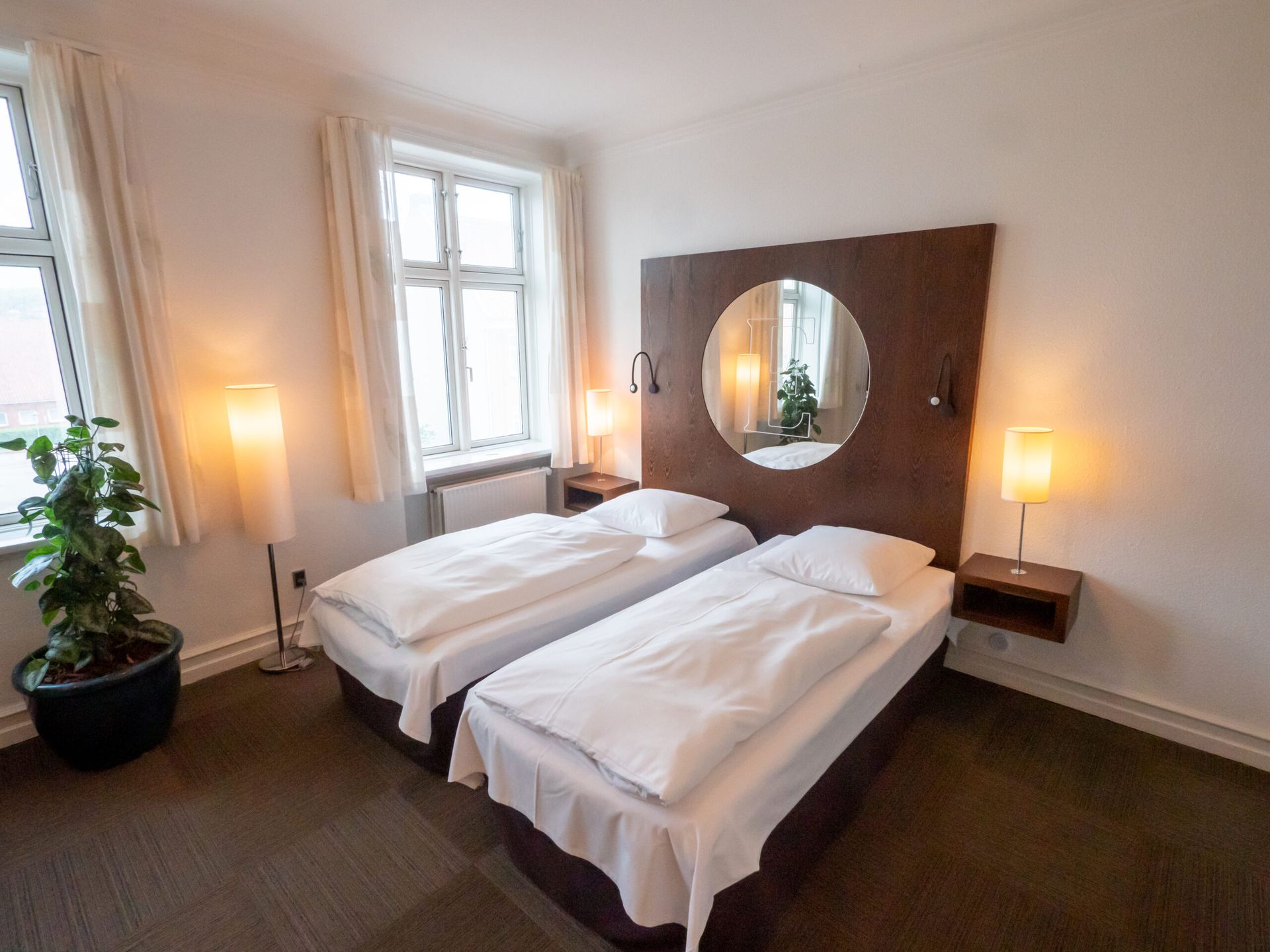 A hotel room with two beds, a large window, and a mirror.