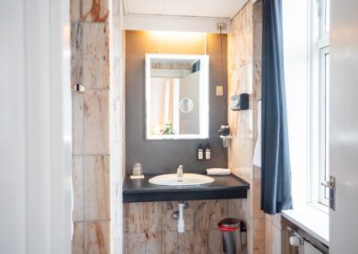 Bathroom with marble walls, dark countertop, sink, and illuminated mirror.  Blue curtain.
