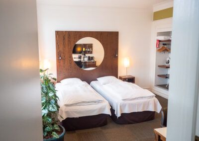 Twin beds in a hotel room, with a round mirror and a small plant.