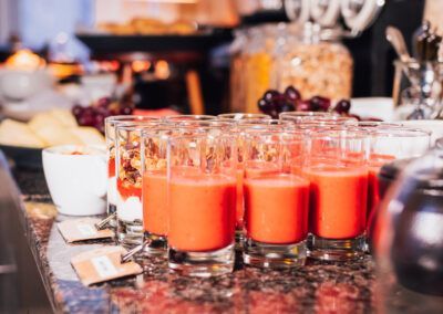 Breakfast buffet with glasses of red juice and other food items.