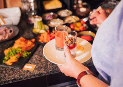 Person holding a plate with two small food glasses, at a buffet with various dishes.