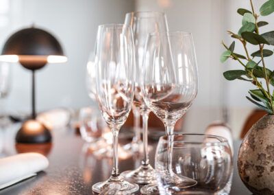 Wine glasses on a table, near a lamp and greenery.