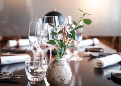 Elegant restaurant table setting with vase of greenery and wine glasses.