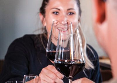 Woman smiling, toasting with two glasses of red wine at a restaurant.