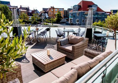 Rooftop patio with wicker furniture, tables, and city view.