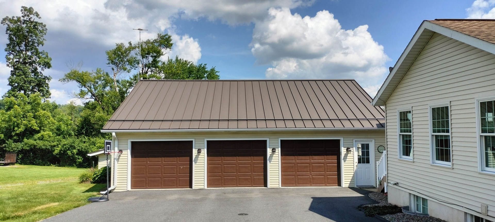 Three-car garage with brown doors and a brown metal roof next to a house with white siding.