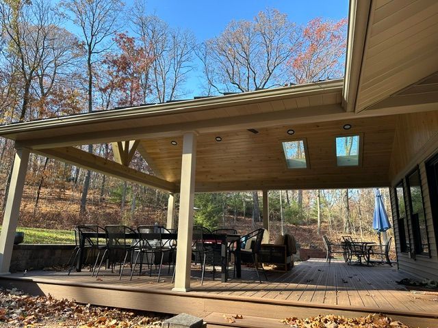 A large covered deck or patio with a table and chairs under a new roof.