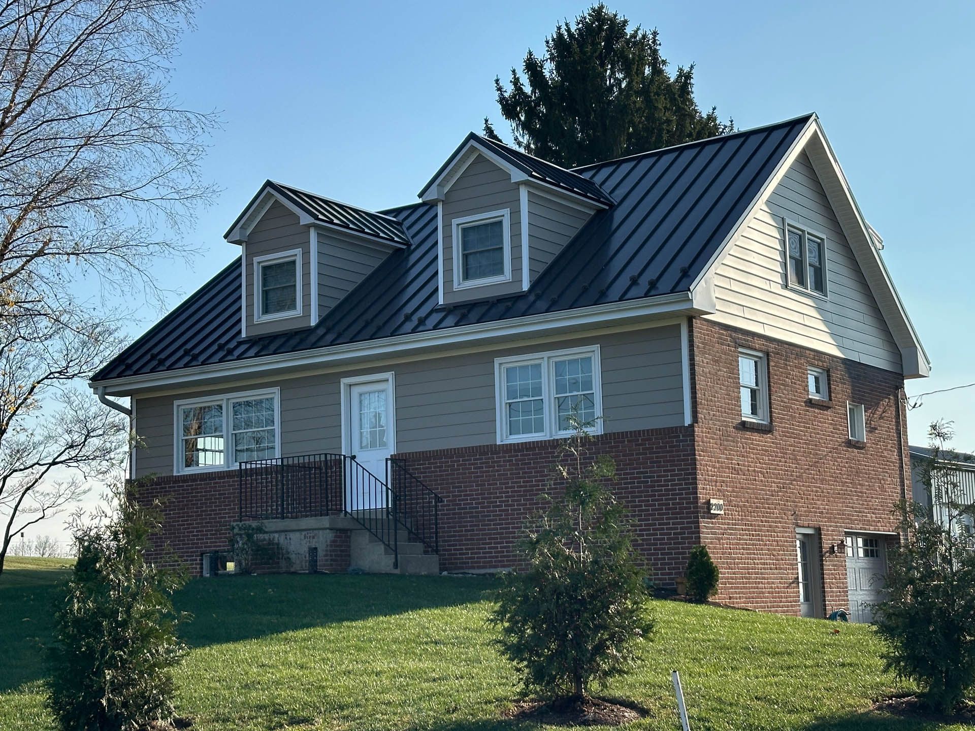 A large brick house with a new black metal roof installed by Sunnyside Roofing