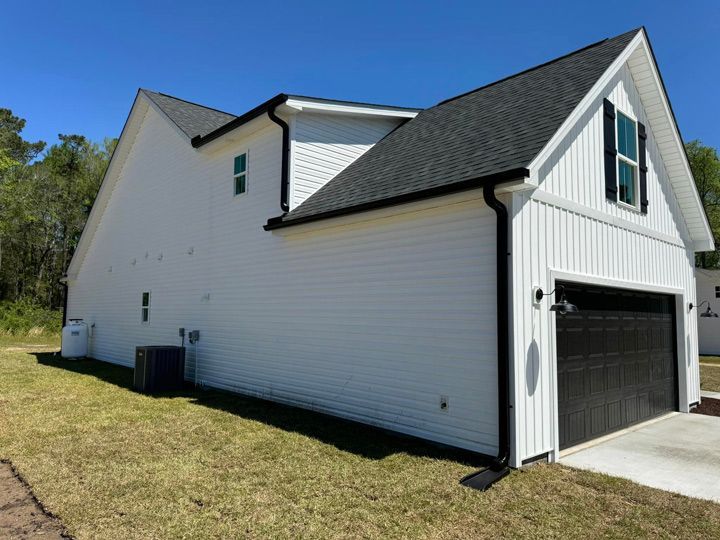 A white house with a black garage door, a black roof, with black seamless gutters.