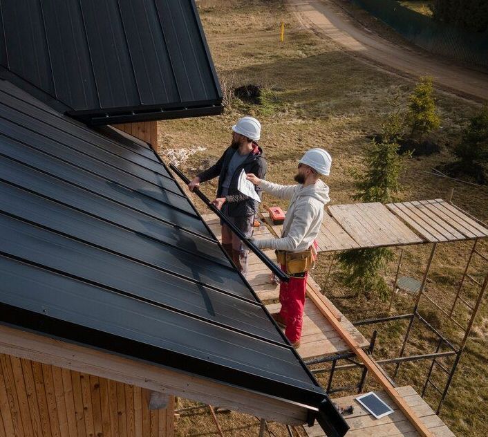 two people are working on the metal roof of a house .