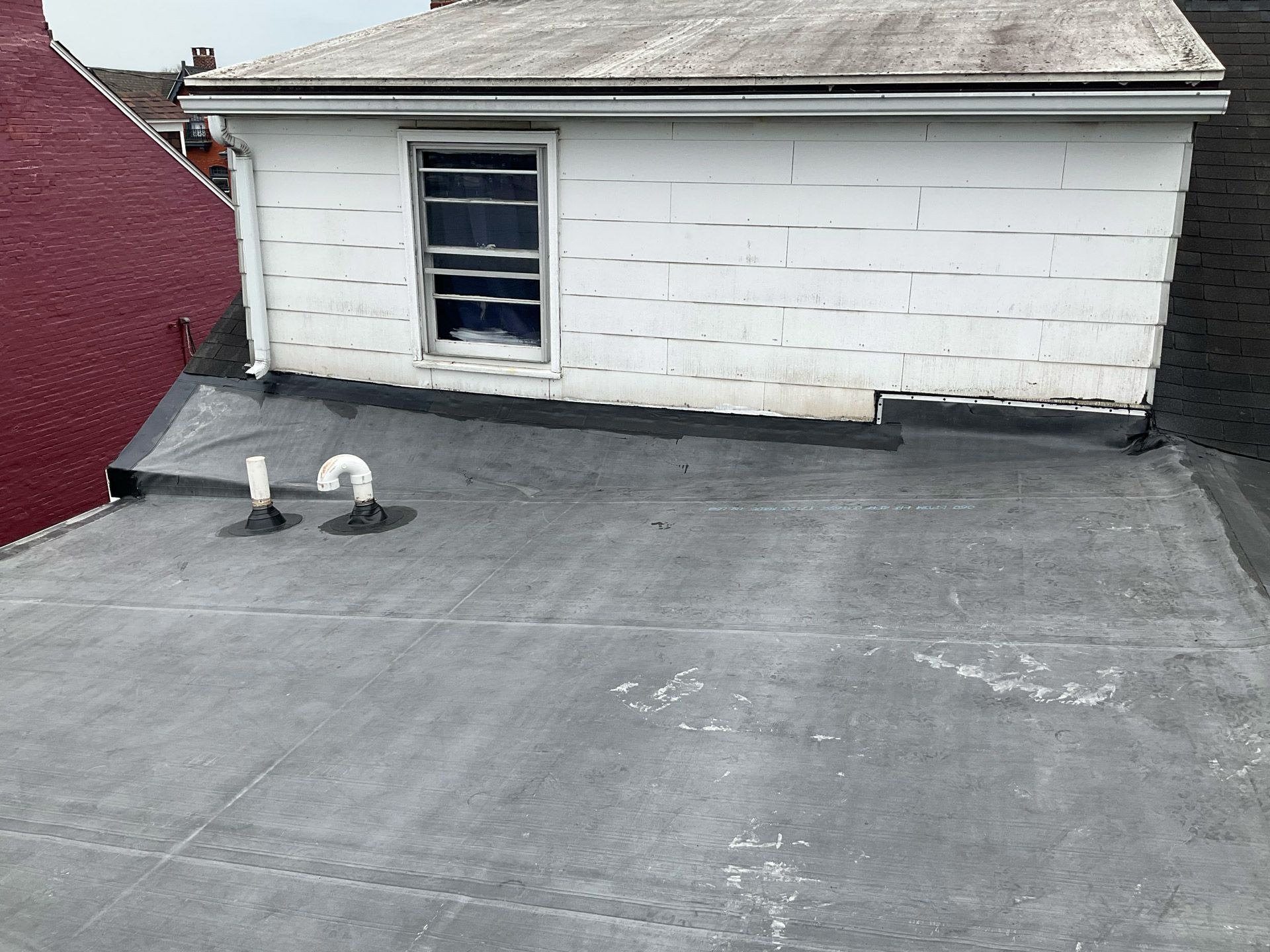 A roof of a house with a window and a pipe on it.