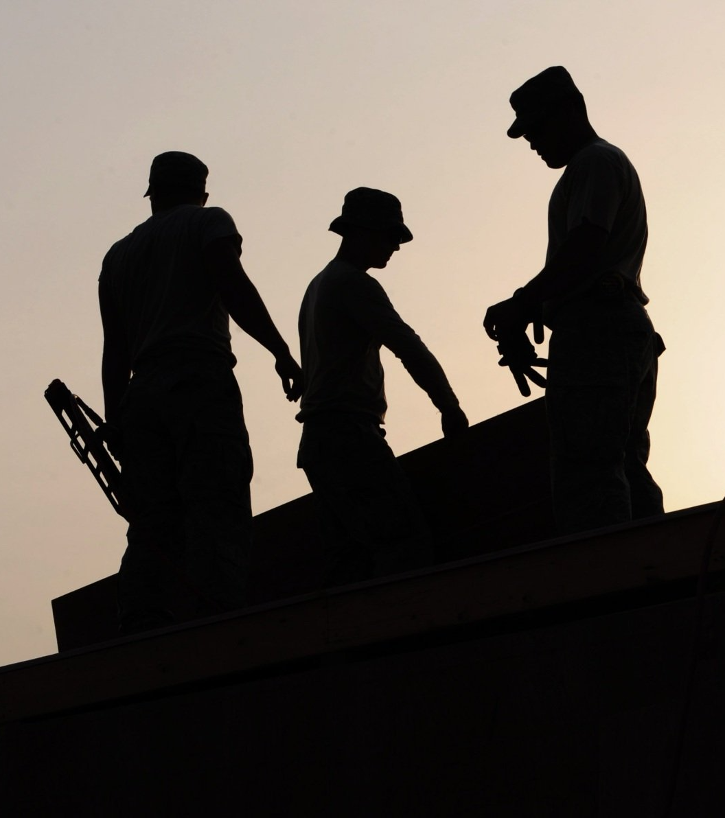 a silhouette of three men standing on top of a building doing roof work