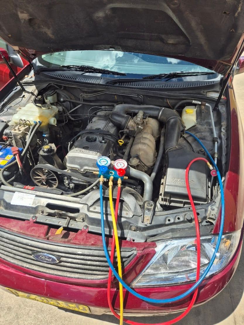 Car engine bay with open hood, red car, air conditioning gauges connected.— Genesis Automotive Services in Lavington, NSW