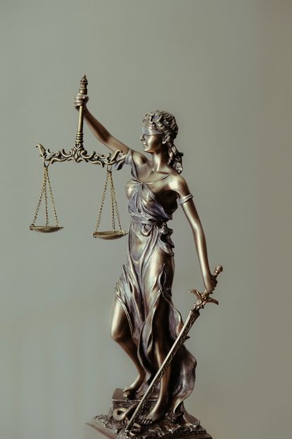 Statue of Lady Justice holding scales in one hand and a sword in the other, on a neutral background.
