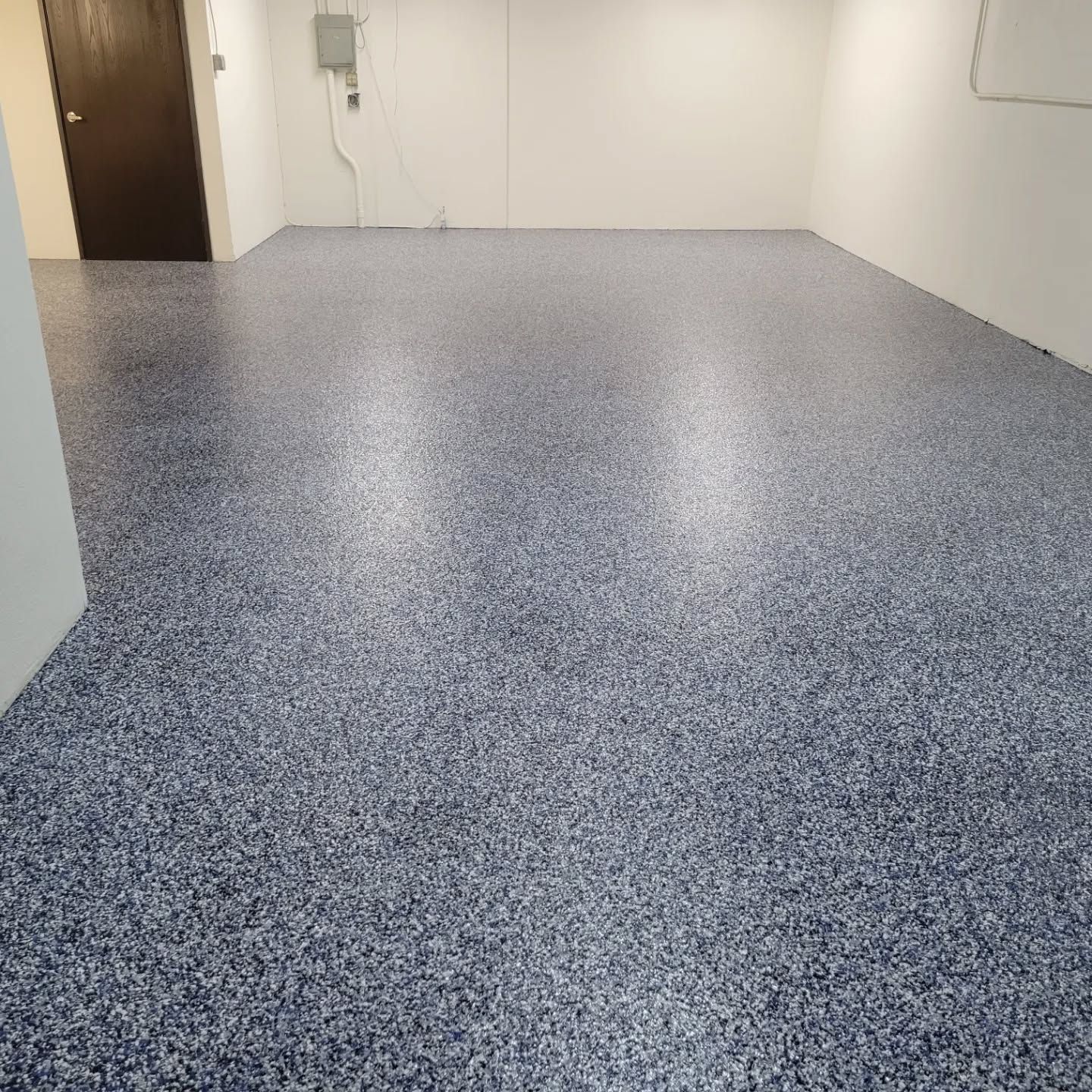 Empty room with speckled blue and gray epoxy floor and white walls. Brown door in the background.