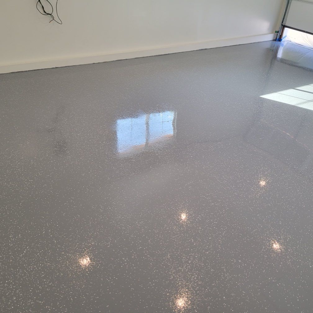 Gray epoxy garage floor reflecting light from a window and ceiling lights.