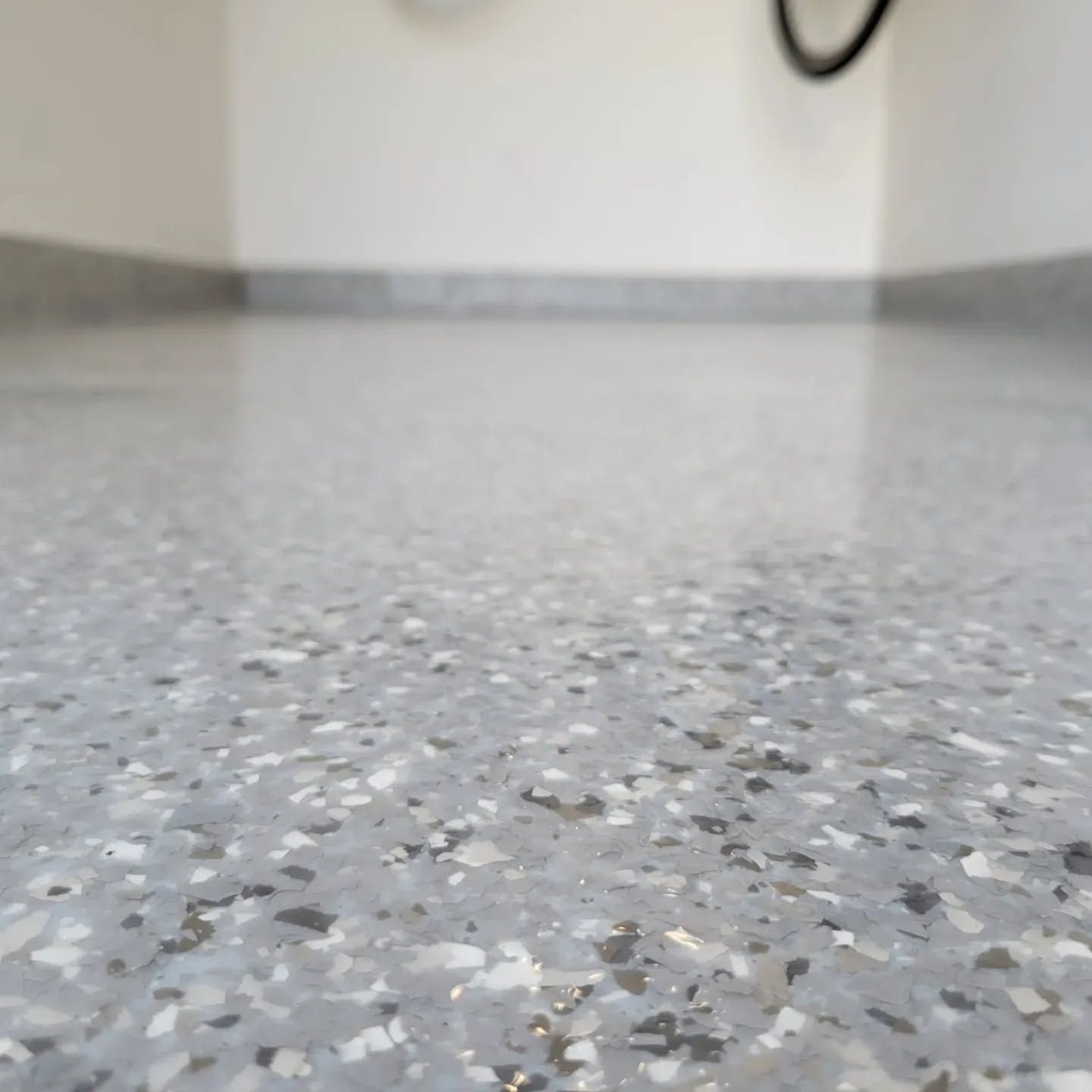 Gray and white speckled flooring with a shiny, reflective surface. The floor meets a white wall.